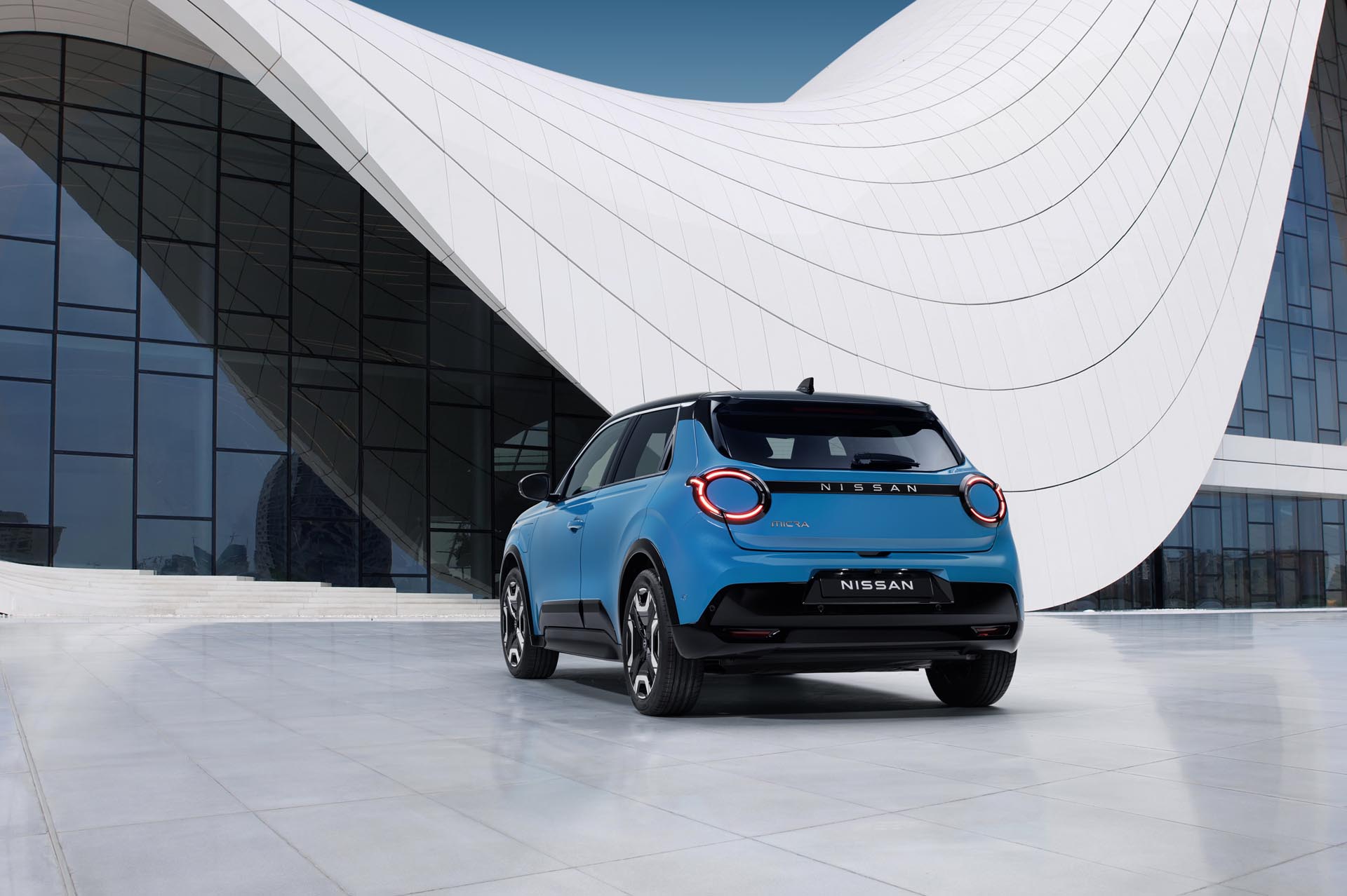 8 view of new Micra in blue gear color in front of a white  blue design architectural building