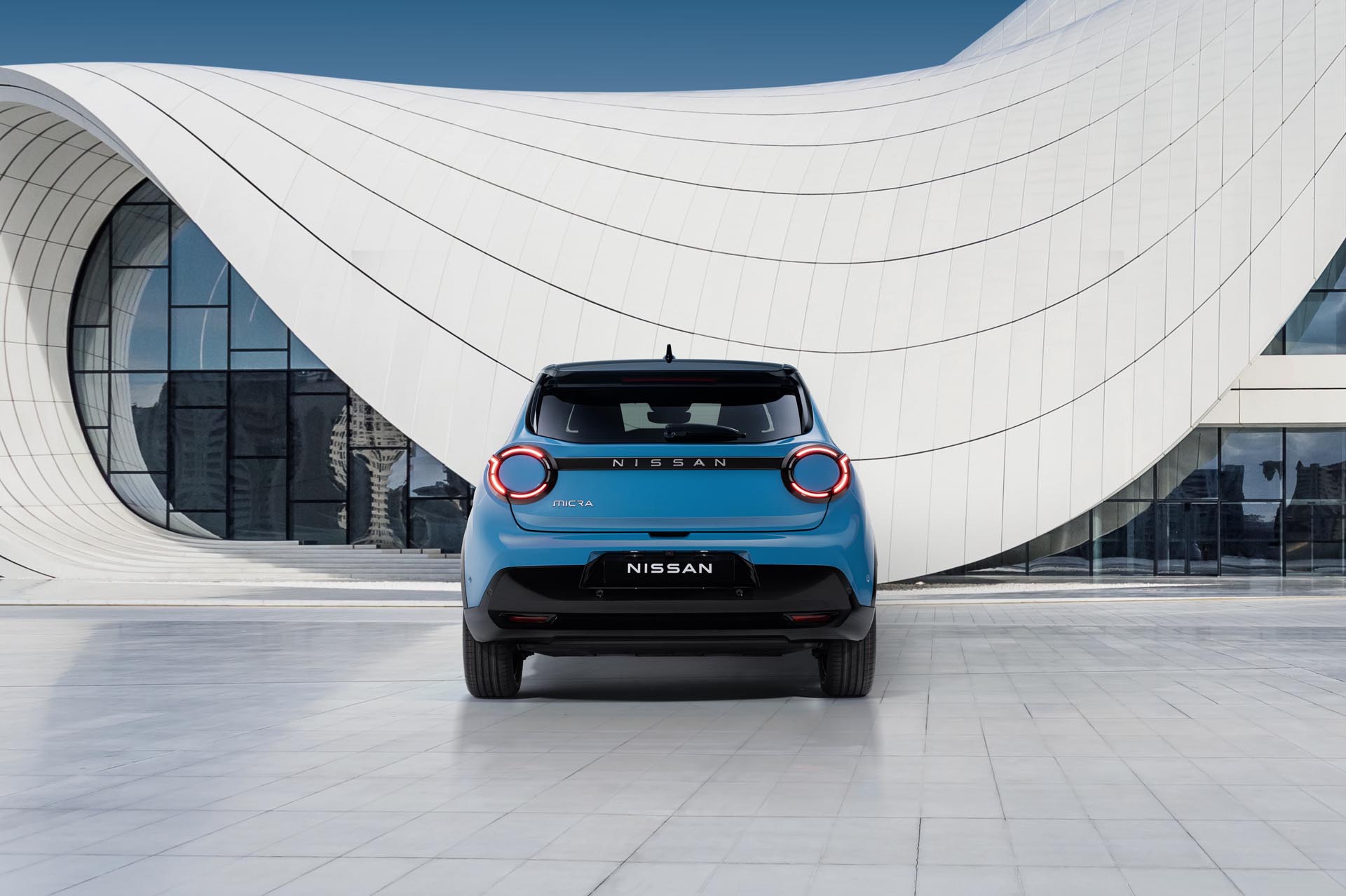 Rear view of gear blue body color  black roof Micra parked in front of a blue  white design architectural building